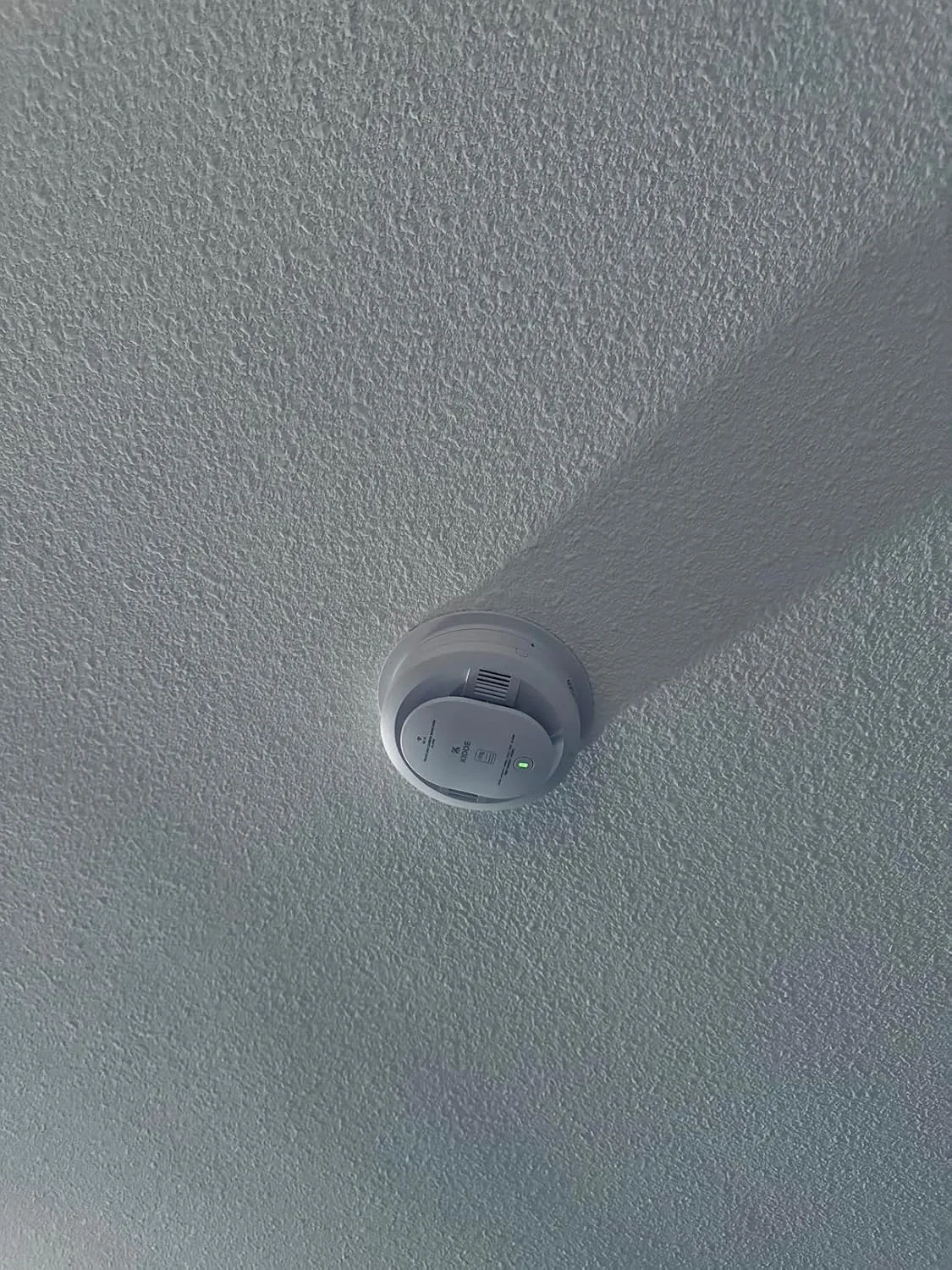 Customer photo of smart smoke alarm mounted on ceiling with mobile app notification displayed