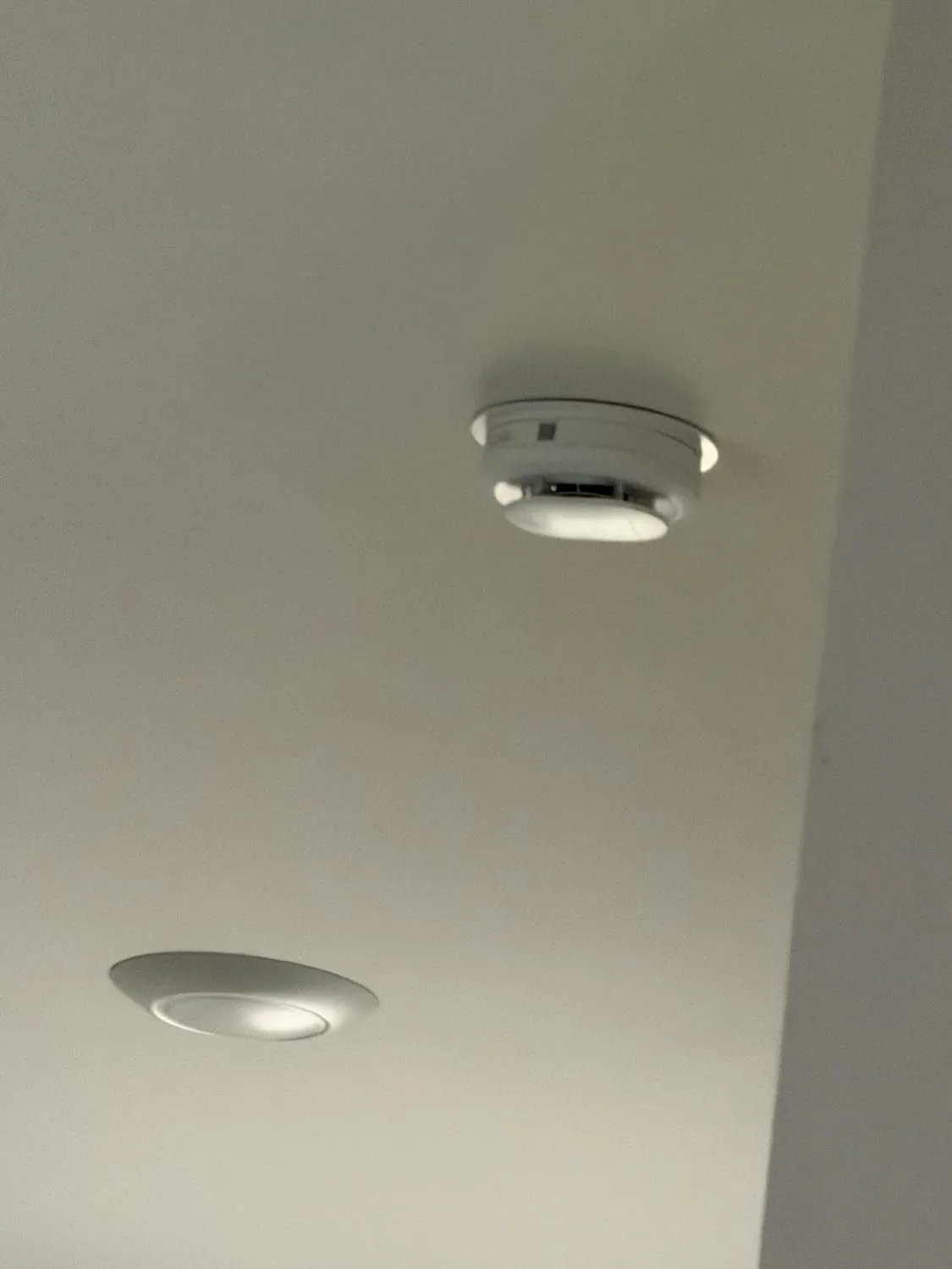 Customer photo of smart smoke alarm mounted on ceiling with mobile app notification displayed